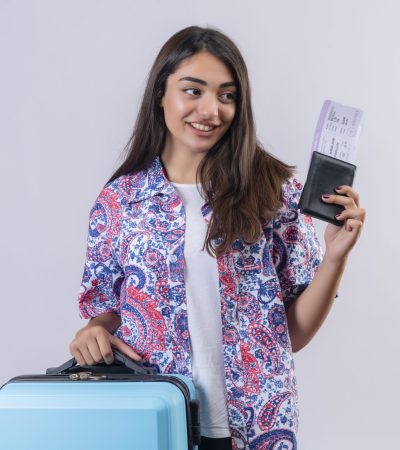 beautiful tourist woman holding travel suitcase and passport with tickets looking aside with smile on face happy and positive travel concept standing over white background